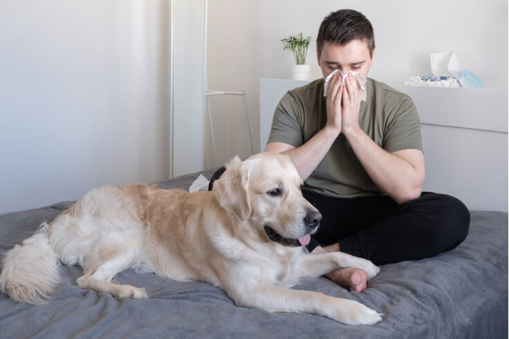 man blowing his nose close to his dog